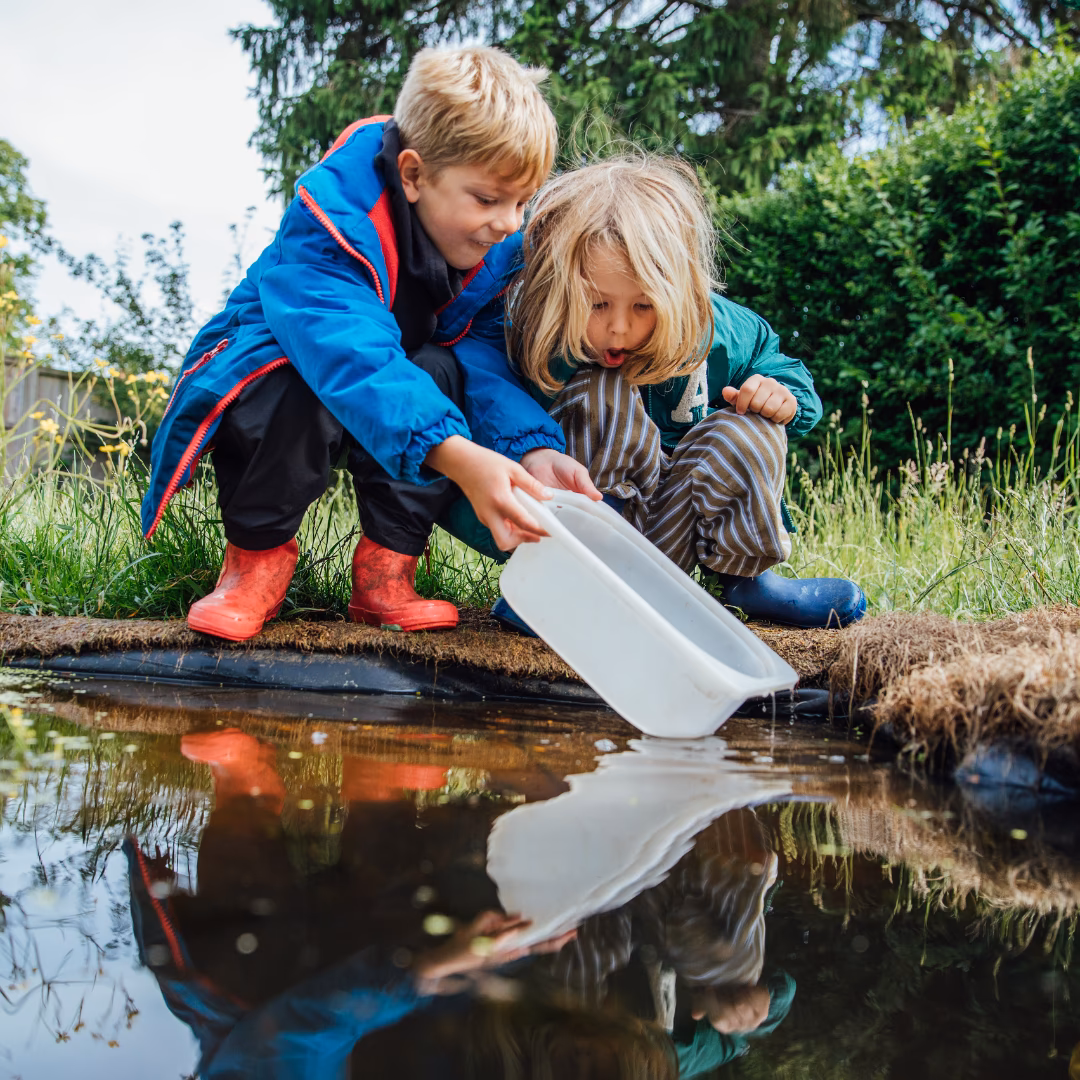 Two children in forest school playing by the pond